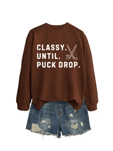 Close-up of coffee brown sweatshirt with Classy Until Puck Drop hockey graphic and denim shorts
