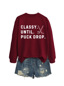 Flat lay of maroon crewneck sweatshirt featuring puck drop slogan with denim shorts