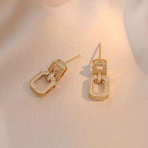 Boucles d'oreilles géométriques dorées avec zircons sur fond de satin champagne