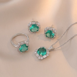 Elegant emerald green jewelry set with silver necklace, ring, and earrings on silk