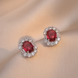 Elegant emerald-cut ruby earrings with surrounding white zircon crystals on silk background
