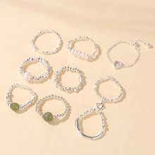 Flat lay of an 8-piece silver beaded ring set with pearls, green stones, and heart charms