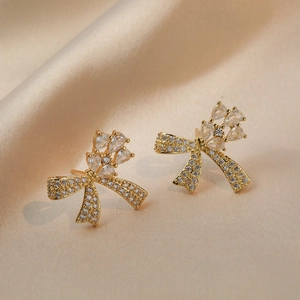 Boucles d'oreilles papillon dorées avec zircons et cristaux sur fond de soie champagne