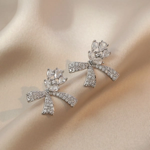 Boucles d'oreilles nœud en argent avec zircons étincelants sur un tissu de soie champagne