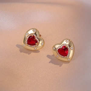 Detail of gold heart earrings with red gemstones and sparkling star engravings