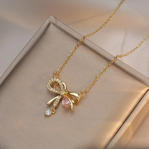 Golden bow necklace with sparkling white zircons and a pink teardrop-shaped gemstone
