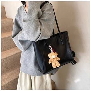 Detail of black tote bag with premium leather texture and a cute teddy bear pendant