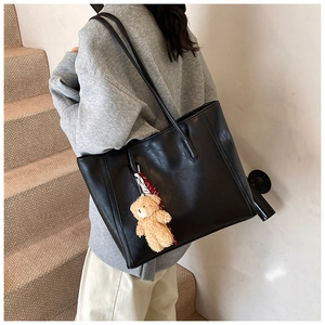 Minimalist black tote bag in soft leather with a cute bear pendant on a model in stairs
