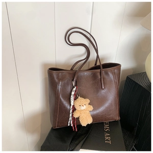 Macro shot of dark brown tote bag with glossy leather texture and plush bear keychain
