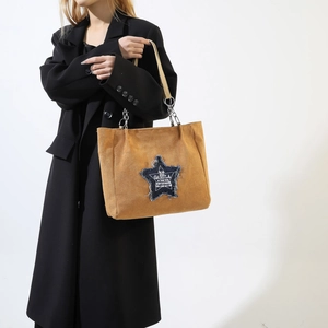 Brown suede tote bag with star patch and metal chain strap shown on model in black coat