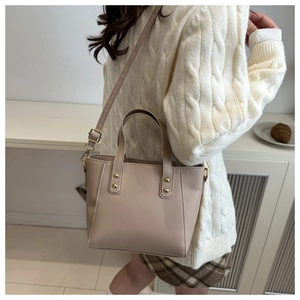 Détail du sac cabas beige en similicuir avec garniture dorée porté sur un pull en maille blanc