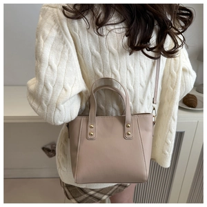 Sac à main beige en simili cuir avec rivets dorés porté par un mannequin dans un salon