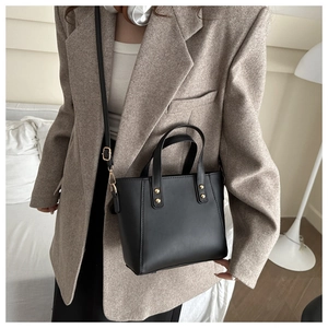 Sac fourre-tout noir minimaliste avec rivets dorés porté par un mannequin élégant
