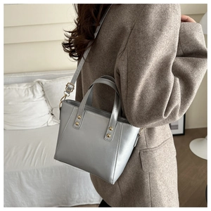 Détail d'un sac à main gris minimaliste porté avec un élégant manteau en laine marron