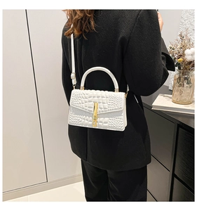 Detailed view of a white crocodile embossed handbag with gold buckle on a black blazer