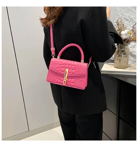 Model wearing a pink crocodile embossed handbag with gold bar and adjustable shoulder strap