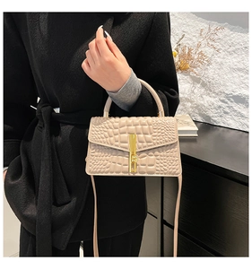 Detail of beige crocodile embossed handbag with golden bar lock and circular top handle