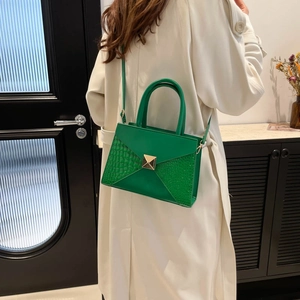 Bright green crocodile pattern envelope handbag worn crossbody by a model in a modern room