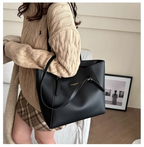 Detail of black leather tote bag with gold metal logo and minimalist trapezoid design
