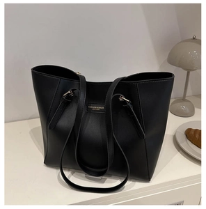 Detail of a large black leather tote bag featuring gold lettering and long shoulder strap