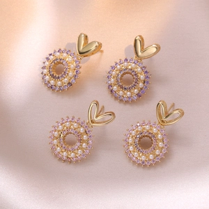 Elegante goldene Herzohrringe mit lila Perlen und Zirkonia auf rosa Seidenhintergrund