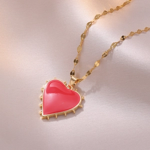Minimalist red heart pendant necklace with gold spiked edge on pink satin background