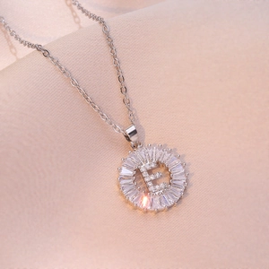 Silver letter E pendant necklace with baguette-cut zircon halo on champagne silk fabric