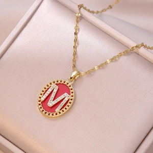 Gold M-letter pendant necklace with red enamel and pavé diamonds in a jewelry box