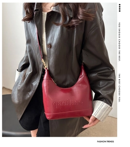Detail of red leather bag with embossed lettering worn by a model in a leather jacket