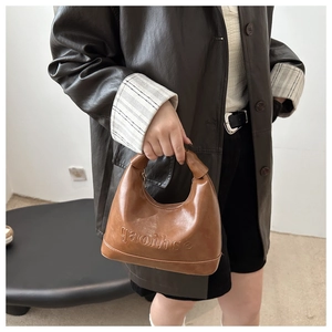 Detail of caramel hobo bag with embossed letters and glossy synthetic leather finish
