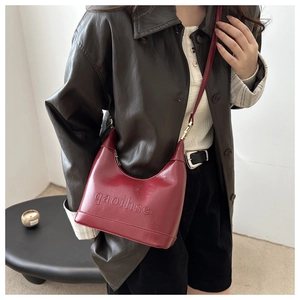Close-up of embossed brand logo on reddish-brown leather crescent shoulder bag detail