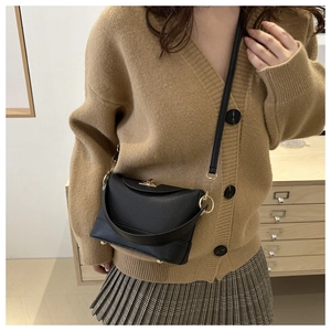 Detail of black pebbled leather crossbody bucket bag with gold clasp shown on model