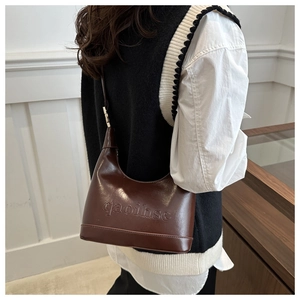 Detail of dark brown leather crescent bag with embossed letters on a model