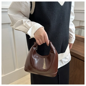 Detail of glossy dark brown leather shoulder bag featuring embossed lettering and fine stitching