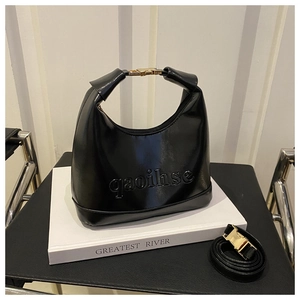 Detailed view of black shiny dumpling bag with embossed letters and gold metal buckle
