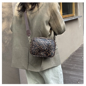 Close-up of leopard print crossbody bag with brown wide strap and gold hardware accents
