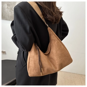 Detail view of brown suede hobo bag featuring wide shoulder strap and tassel drawstring