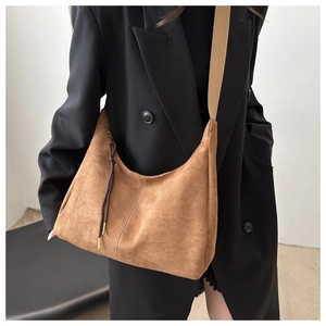 Detail of caramel suede hobo bag with fringe and wide woven strap on a black blazer