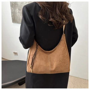Brown suede half-moon bag worn on shoulder by model in a black tailored blazer
