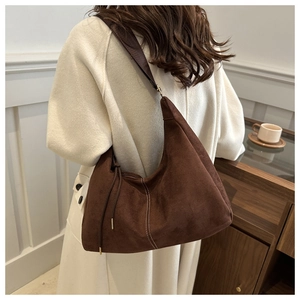 Detail view of retro brown suede hobo bag featuring white stitching and tassel charm