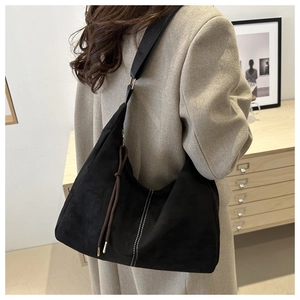 Close-up of black suede underarm bag with white stitching and wide shoulder strap