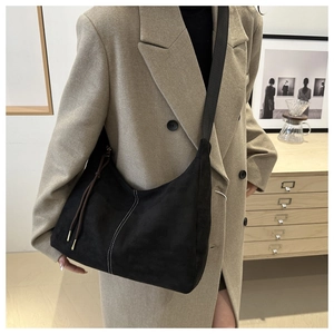 Detail of black suede hobo bag with contrast stitching and shoulder strap on model