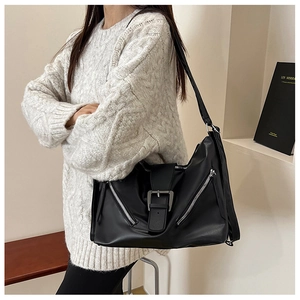 Détail du sac hobo noir avec boucle argentée et fermetures éclair porté sur un pull blanc