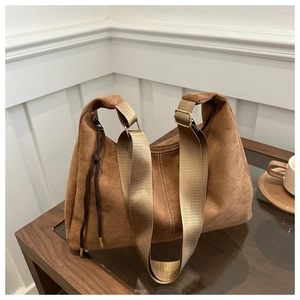 Detailed shot of brown matte suede shoulder bag with side drawstrings on a glass table