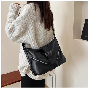 Gros plan d'un sac bandoulière noir avec boucle argentée porté sur un pull en maille blanc