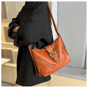 Sac bandoulière en cuir caramel avec zips métalliques et boucle porté par un modèle