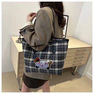 Détail du sac cabas à carreaux avec une broderie de chien sur un tissu gris texturé