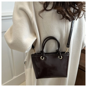 Glossy dark brown leather bucket bag with top handles and gold hardware on model