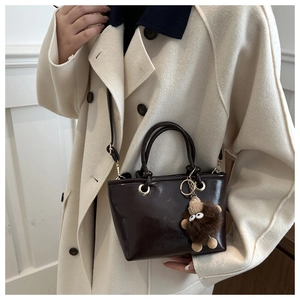 Detail of dark brown glossy patent leather bucket bag with cute plush bear charm