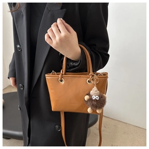 Brown leather bucket bag with fuzzy charm and embossed text worn on black coat